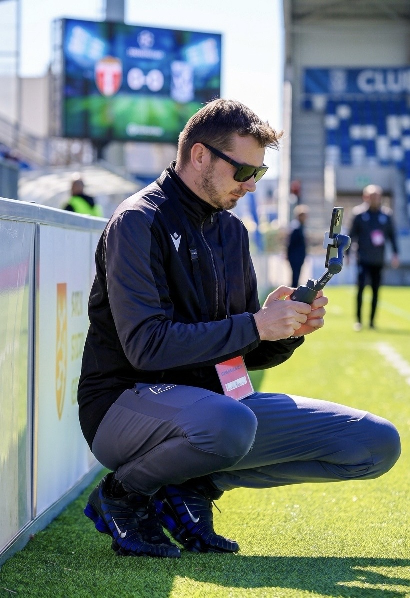 Lukáš Řezníček v bílé mikině natáčí telefonem na gimbalu u fotbalového hřiště